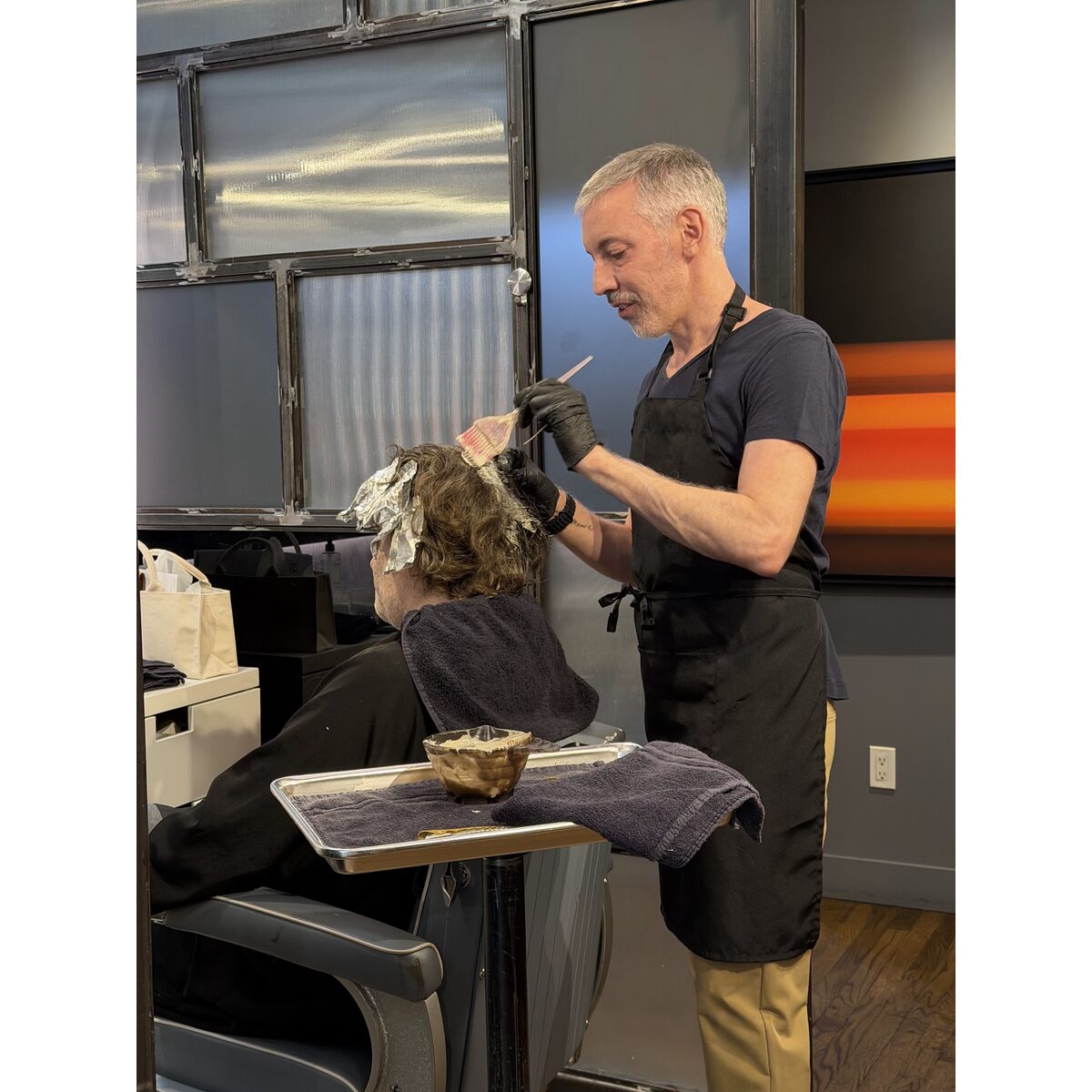 A colorist painting color through a guest’s hair with a tint brush — gray blending in progress at Martial Vivot Salon Pour Hommes